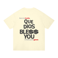 A pale cream-colored t-shirt shown from the back, featuring a Spanish graphic print that reads 'Born to hustle. QUE DIOS BLESS$ YOU / Criado para ganar.