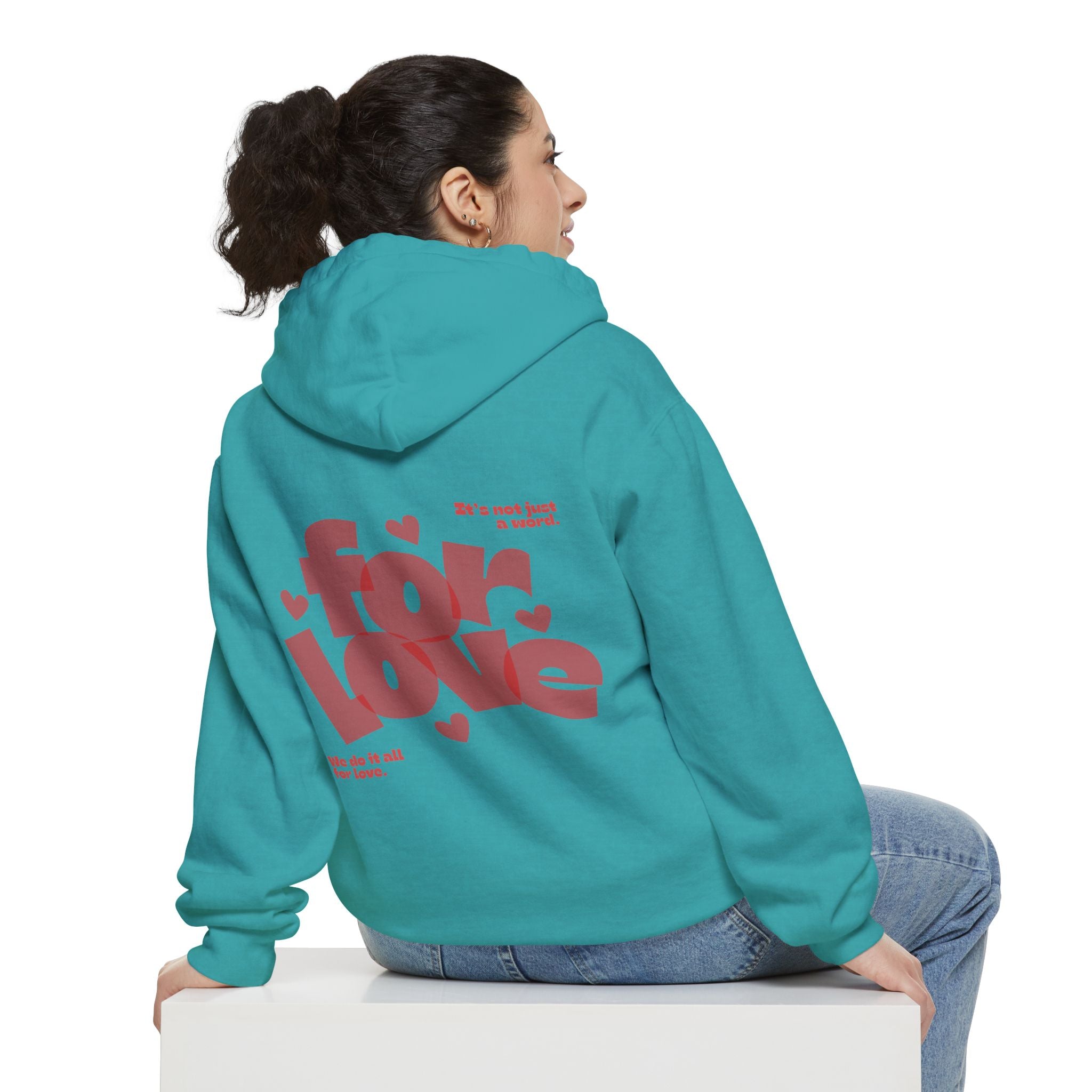 Person wearing a teal hoodie with red text on the back, sitting on a white cube.