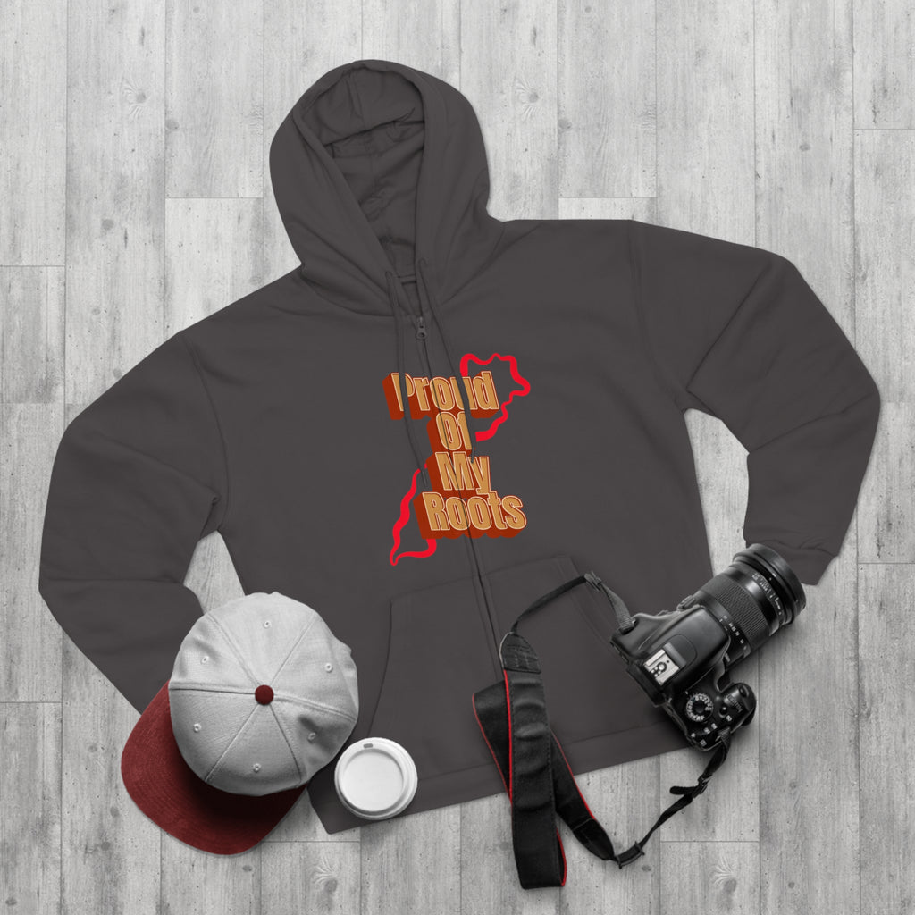 Dark gray hoodie with 'Proud of My Roots' design, white cap, red hat, white cup, and camera on a wooden surface.