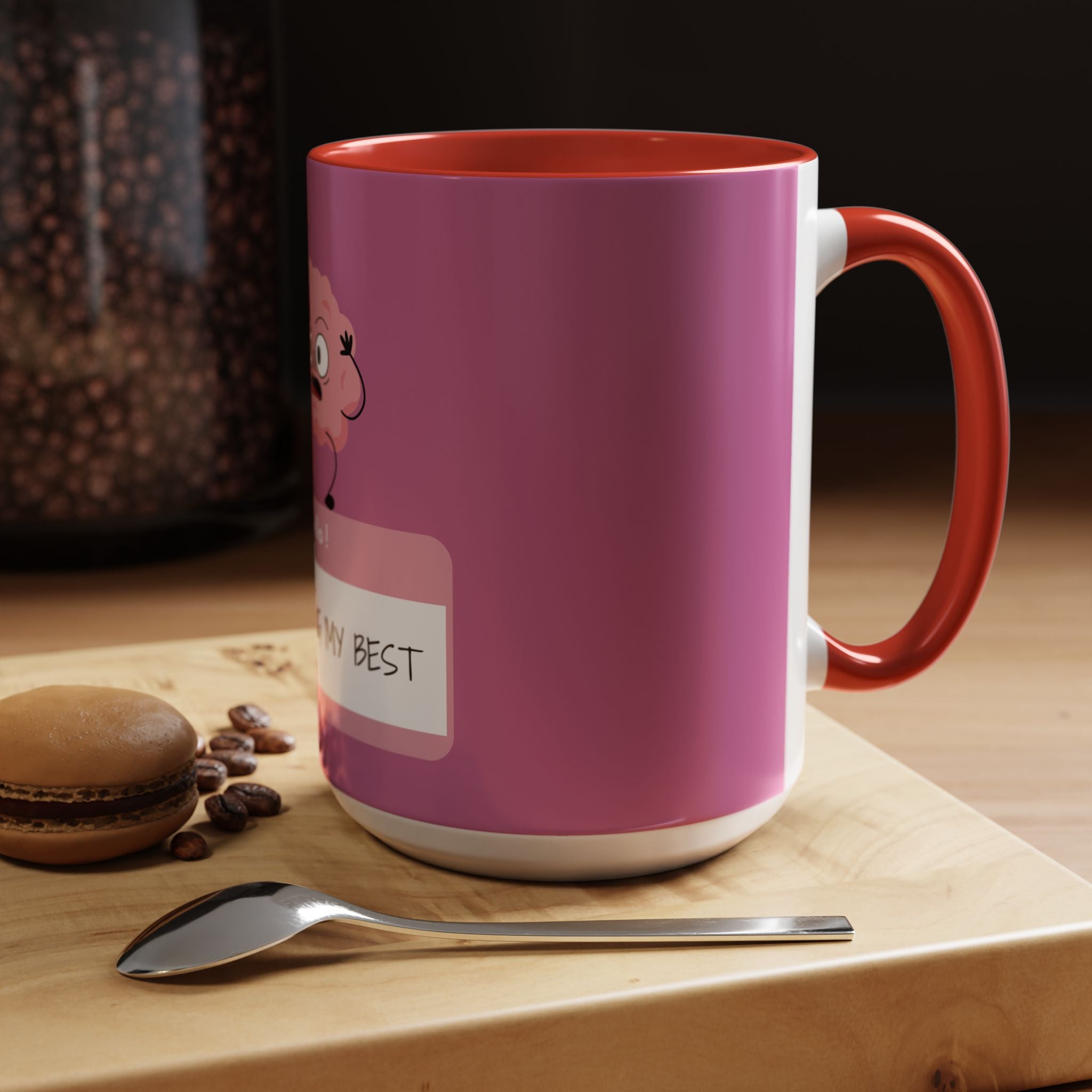 Pink mug with cartoon character and text on a wooden surface with coffee beans and a macaron.