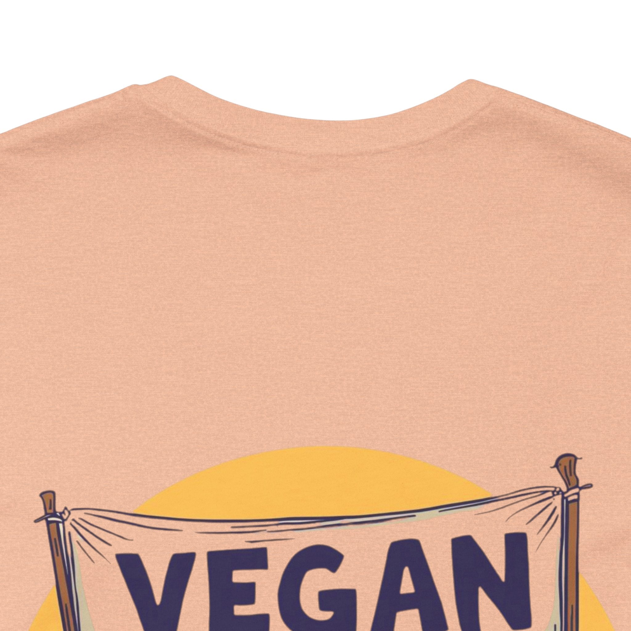 Beige t-shirt with 'VEGAN' banner design on a plain background