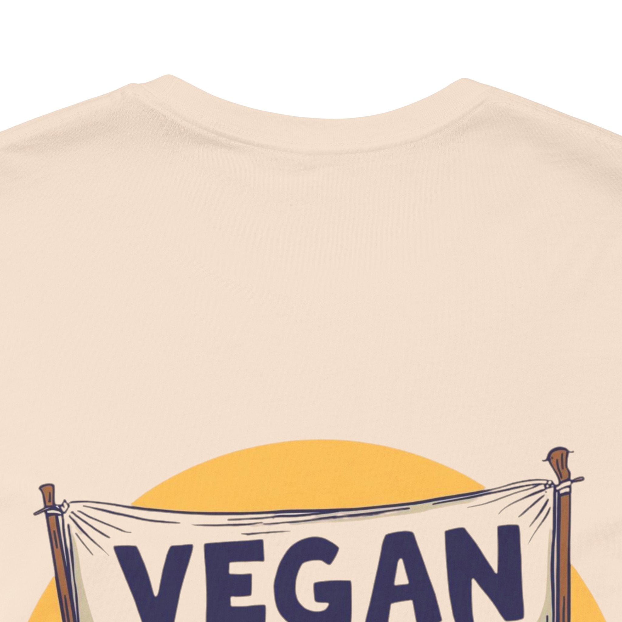 Beige t-shirt with 'VEGAN' banner graphic on a plain background
