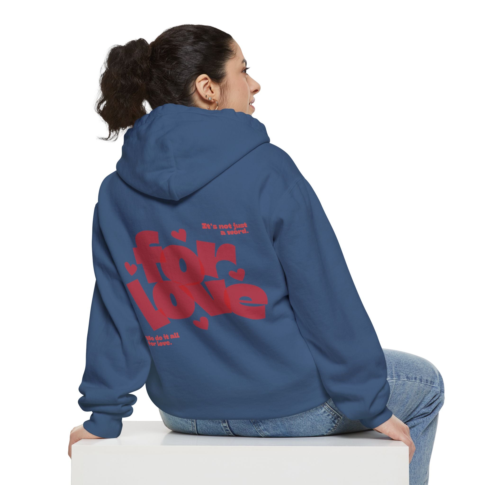 Person wearing a blue hoodie with red text on the back, sitting on a white cube against a white background