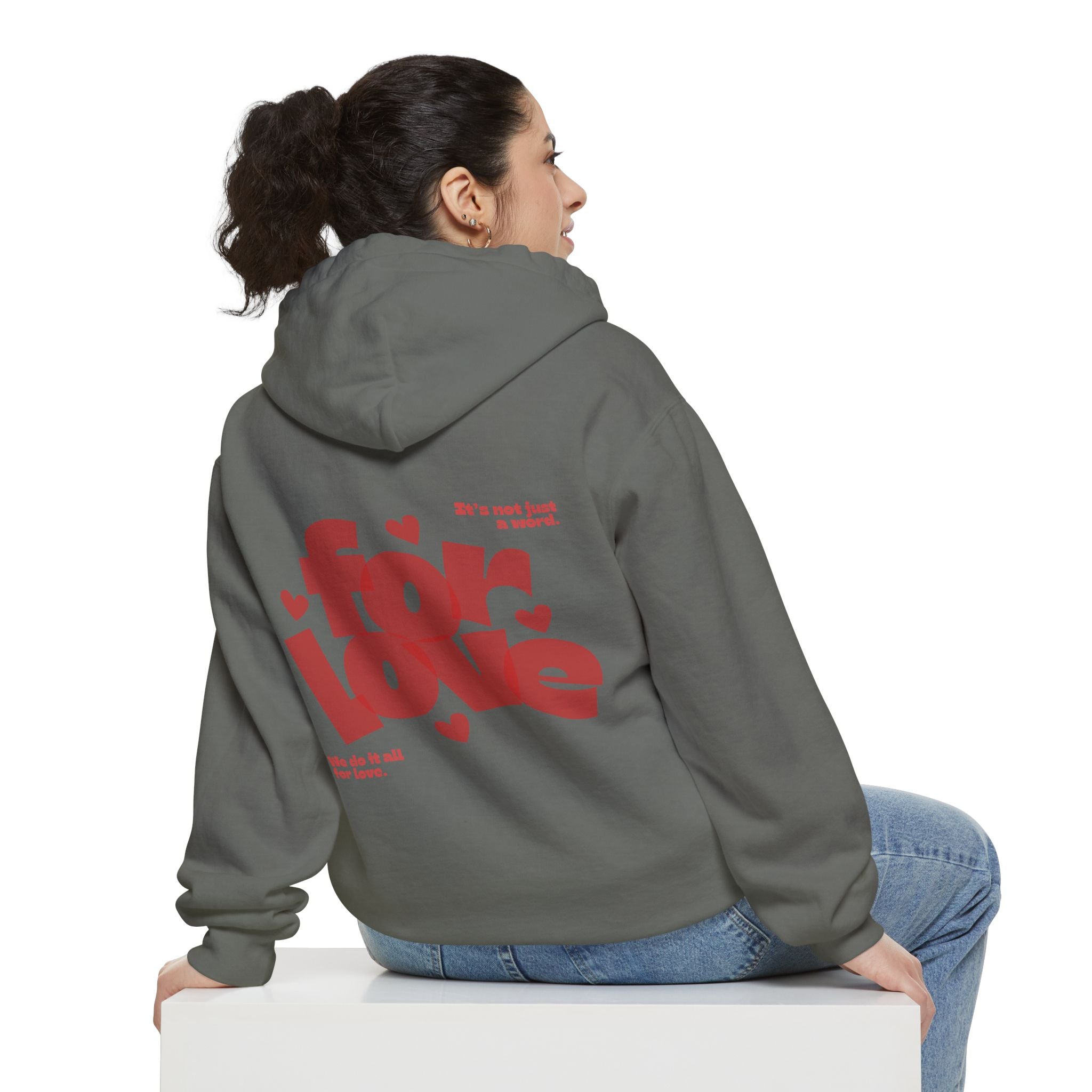 Person wearing a gray hoodie with red text on the back, sitting on a white box against a white background