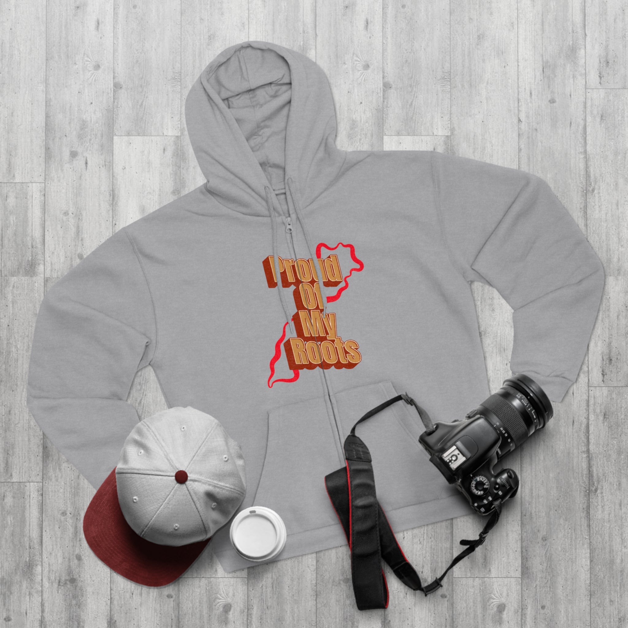 Gray hoodie with text, white cap, white mug, and camera on a wooden surface