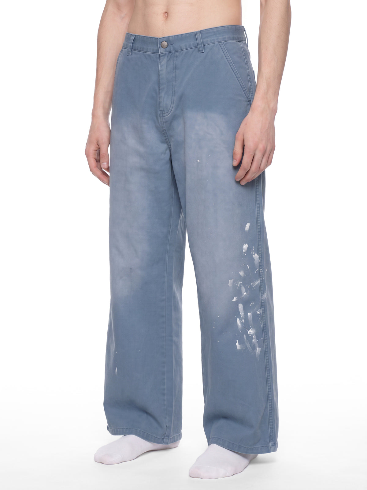 A model wearing wide-leg light blue denim jeans with white paint splatter details on the front and right leg, paired with white socks against a plain white background.