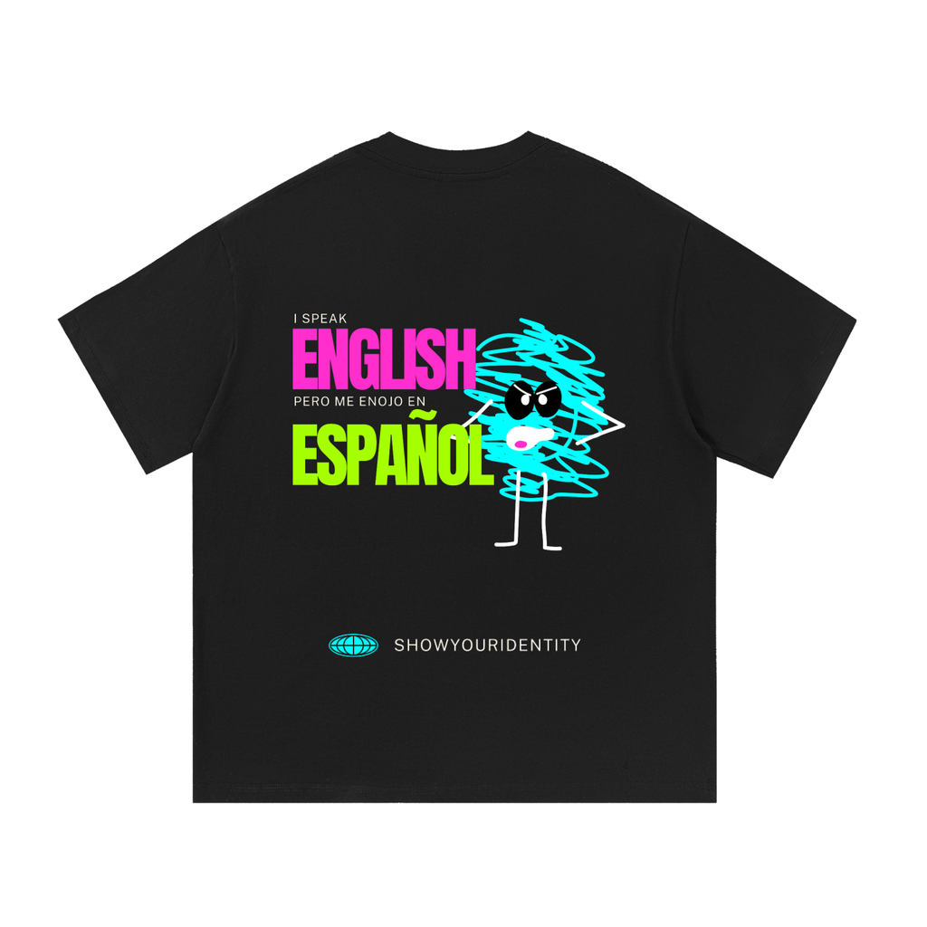 A black short-sleeve t-shirt shown flat against a white background, featuring a colorful graphic on the front with the text 'I SPEAK ENGLISH PERO ME ENJOY EN ESPAÁOL' and a cartoon character made of scribbled lines. The brand name 'SHOWYOURIDENTITY' is printed below the graphic.