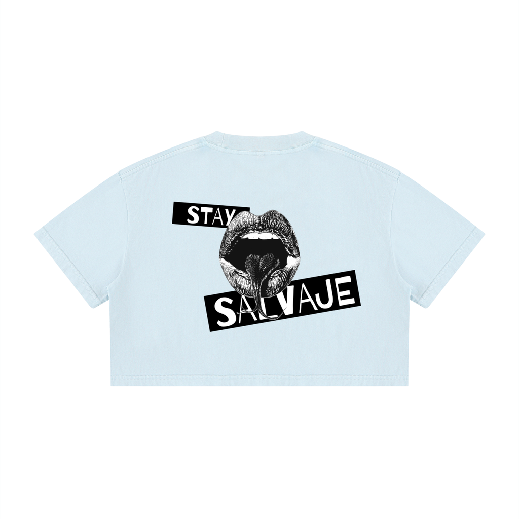 Un *crop top* de manga corta en color azul claro, visto desde atrás, que presenta un gráfico negro de una boca abierta con la lengua visible y las palabras «STAY SALVAJE» impresas en el centro.