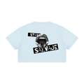 Un *crop top* de manga corta en color azul claro, visto desde atrás, que presenta un gráfico negro de una boca abierta con la lengua visible y las palabras «STAY SALVAJE» impresas en el centro.