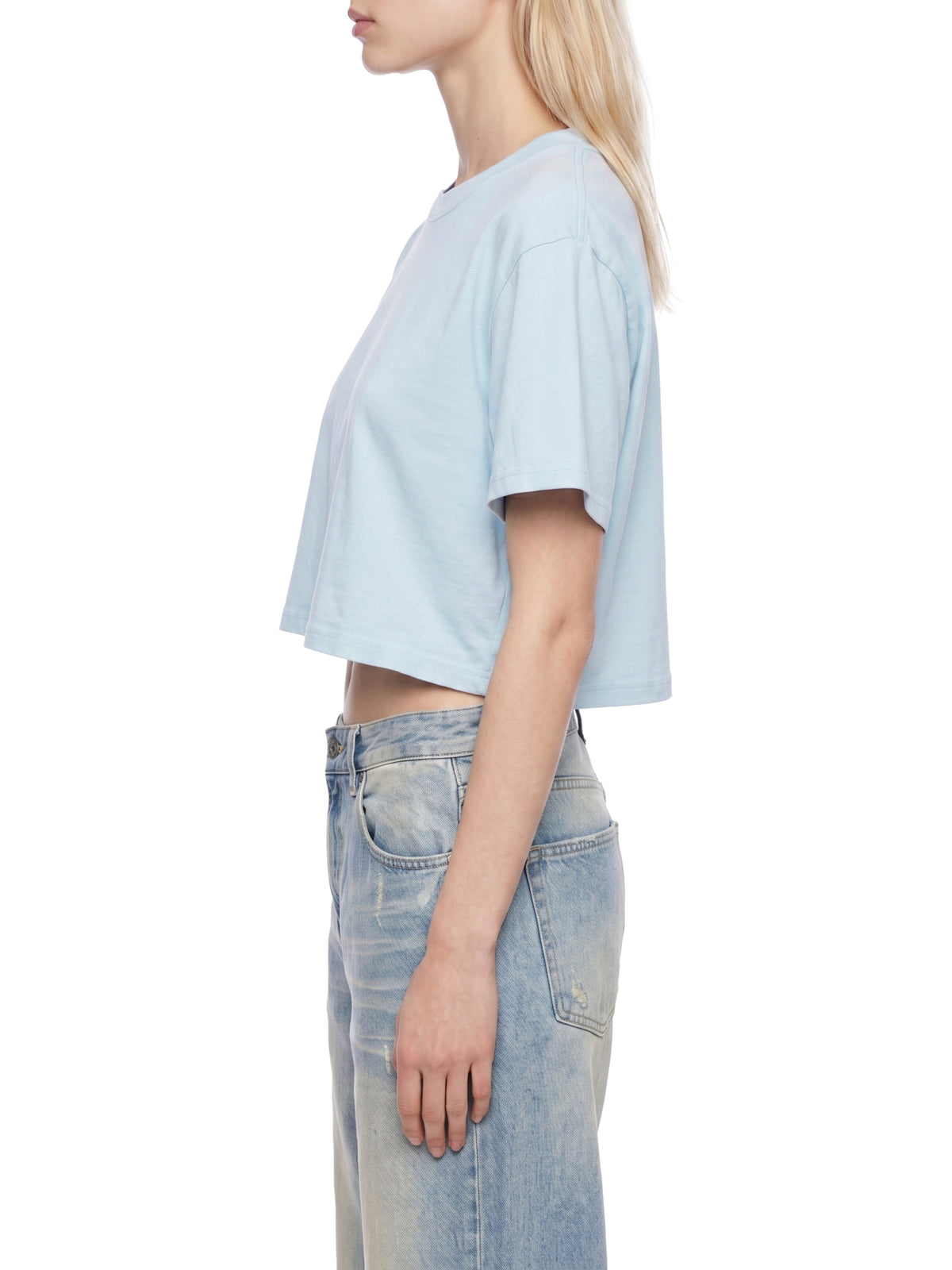 Persona con camiseta azul claro y vaqueros sobre fondo blanco.