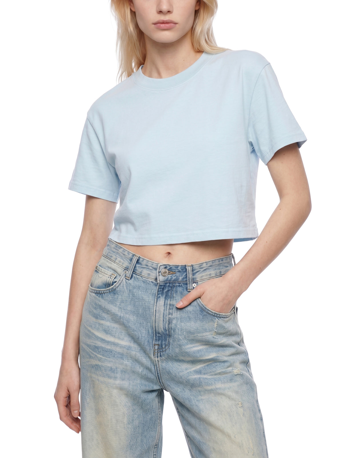Persona con una camiseta corta azul claro y vaqueros sobre un fondo blanco.