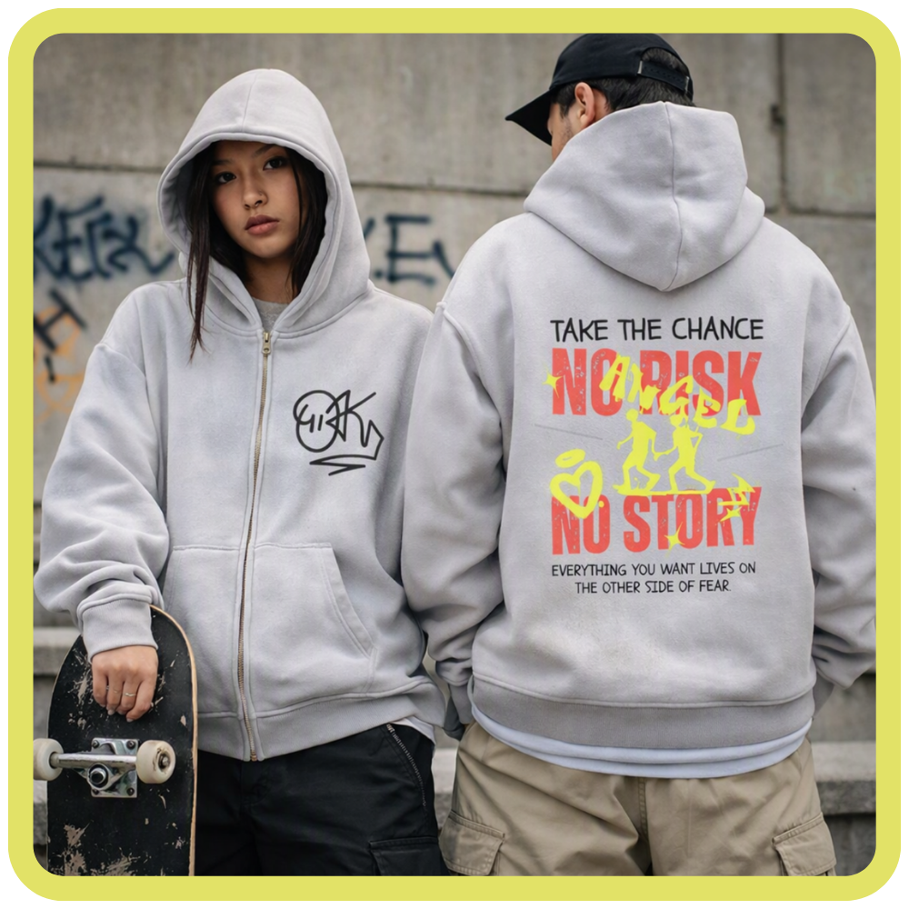Two models wearing light gray zip-up hoodies in an outdoor urban setting. The model on the left shows the front of the hoodie with a black graphic logo, while the model on the right shows the back of the hoodie with a large red, yellow, and black graphic reading 'NO RISK NO STORY'.