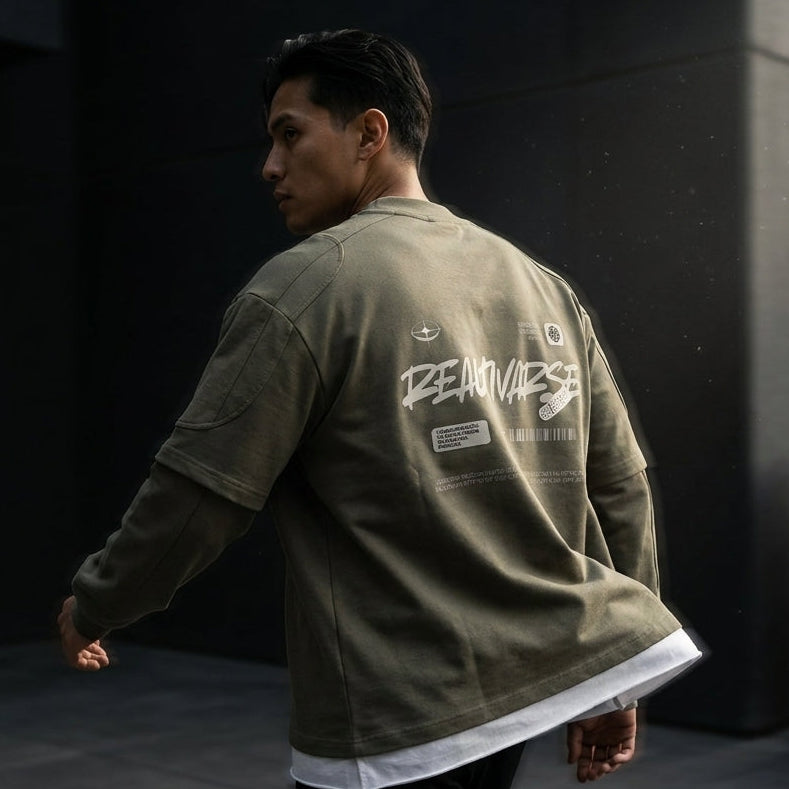 A man wearing an olive green oversized jacket with a white graphic print on the back, walking in a dark modern outdoor setting.